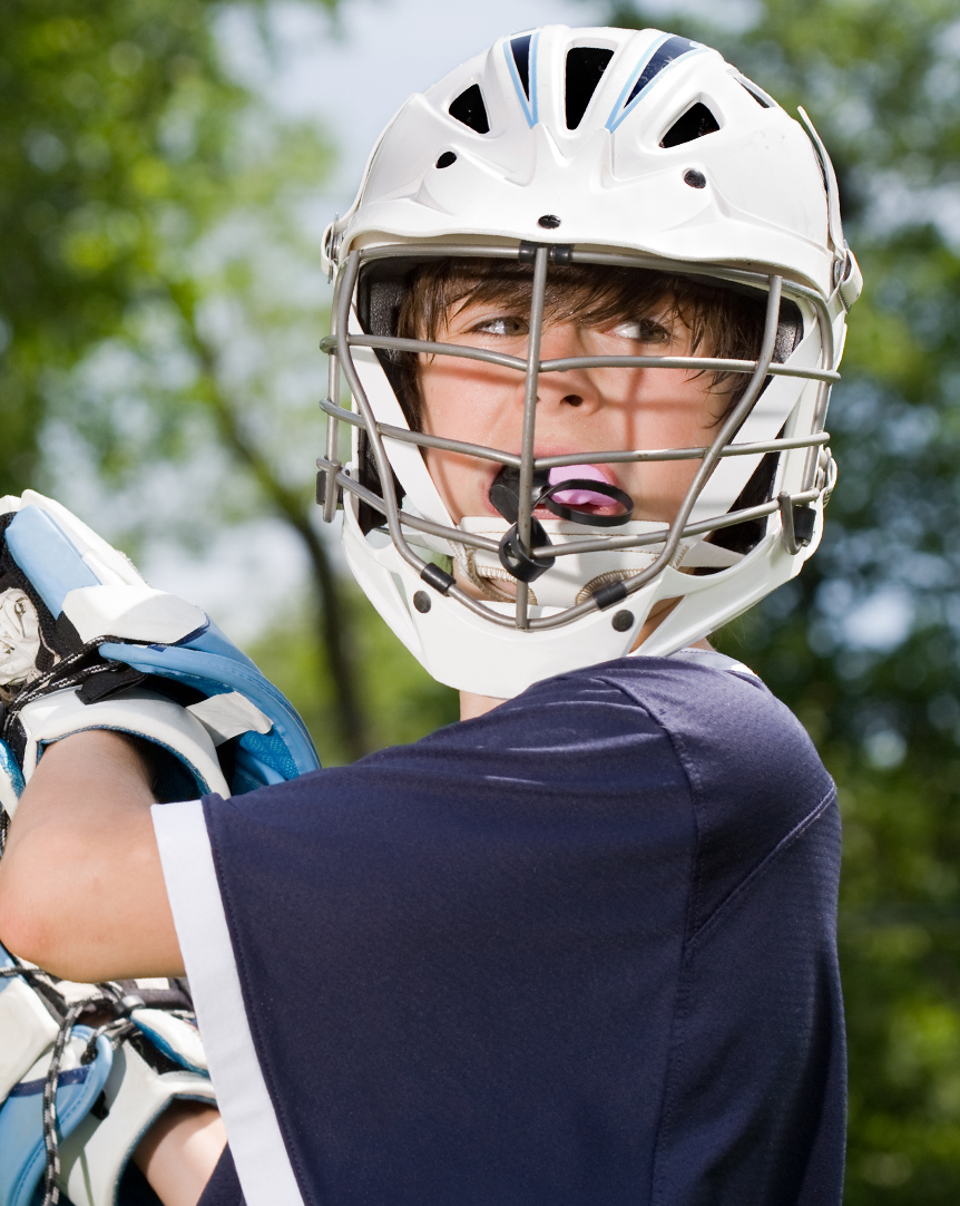 young boy playing lacrosse with a mouthguard in